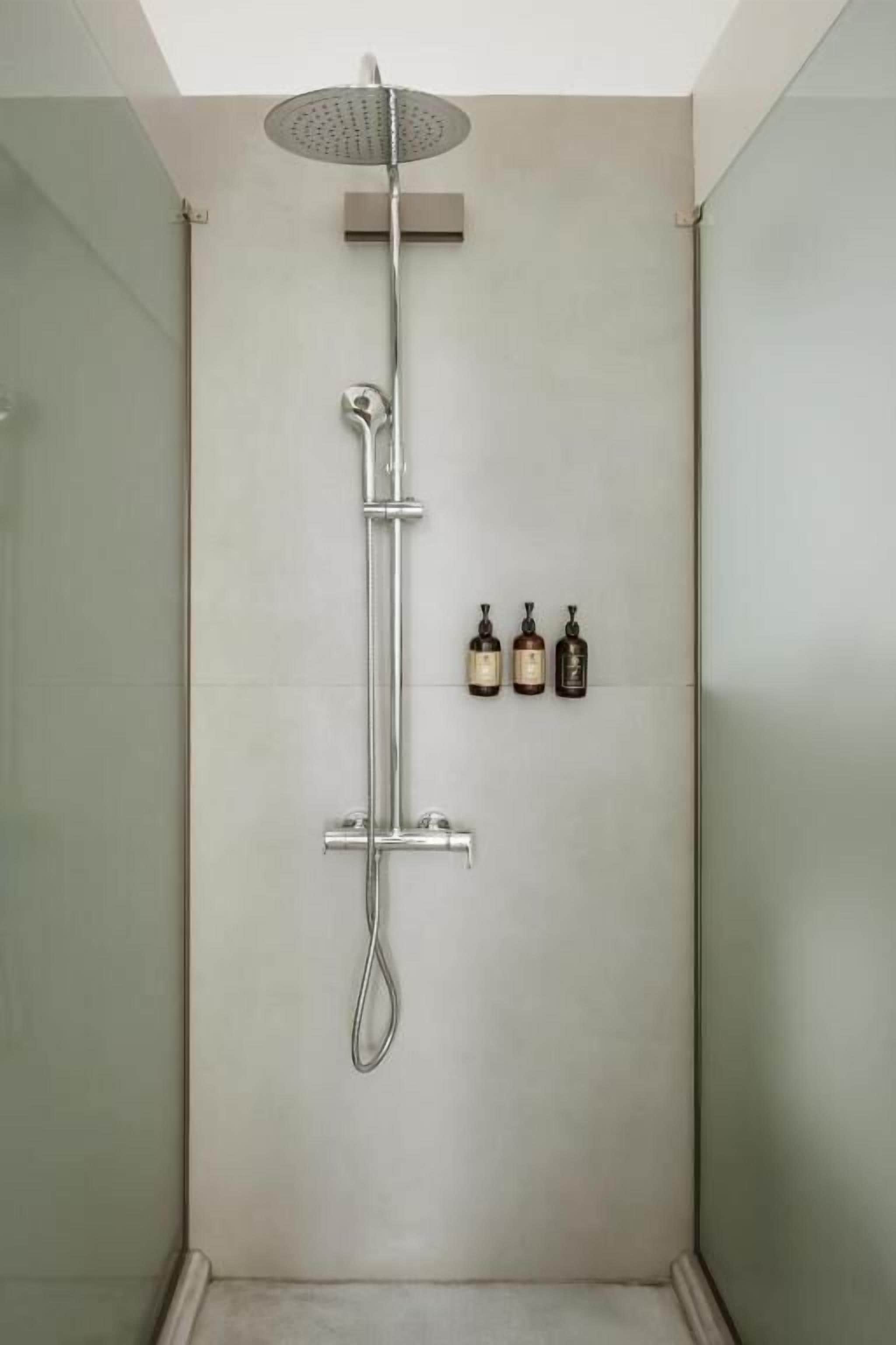 Chuveiro com chuveiro manual e torneira fixada na parede. Há três frascos de shampoo e condicionador na parede.