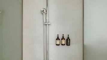 Chuveiro com chuveiro manual e torneira fixada na parede. Há três frascos de shampoo e condicionador na parede.
