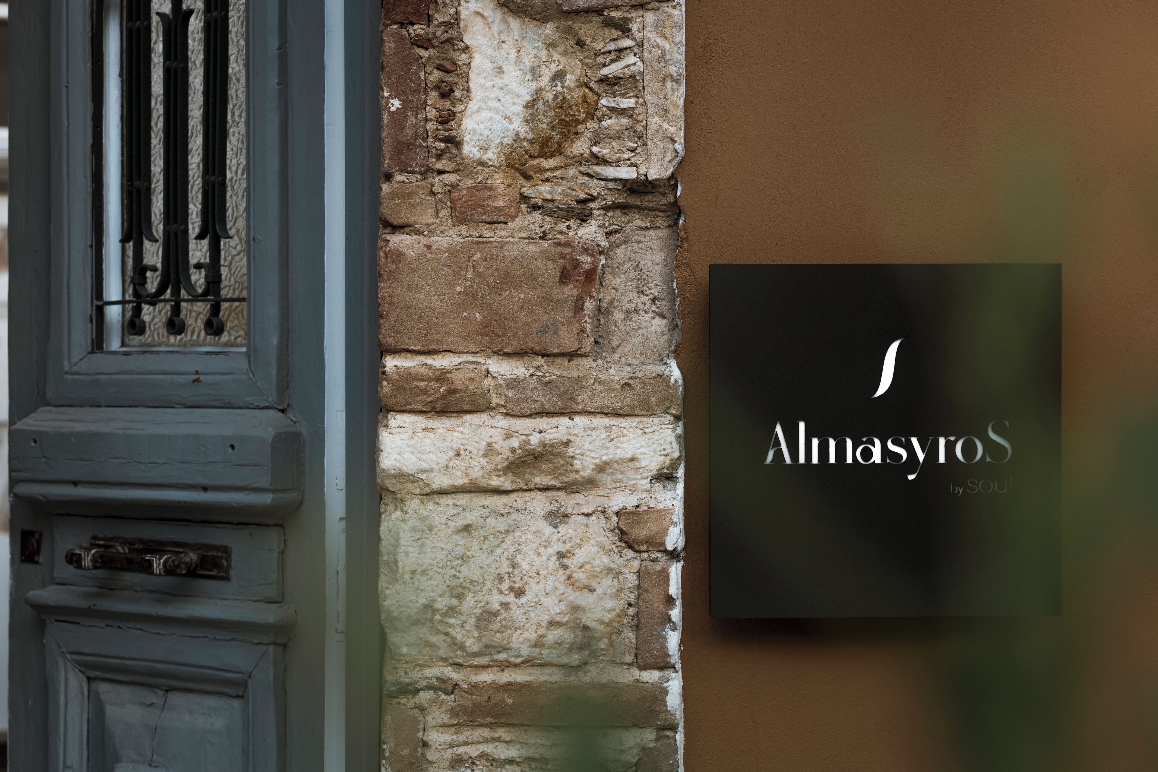 A rustic brick wall with a black sign that reads "Almasyros by Soul."