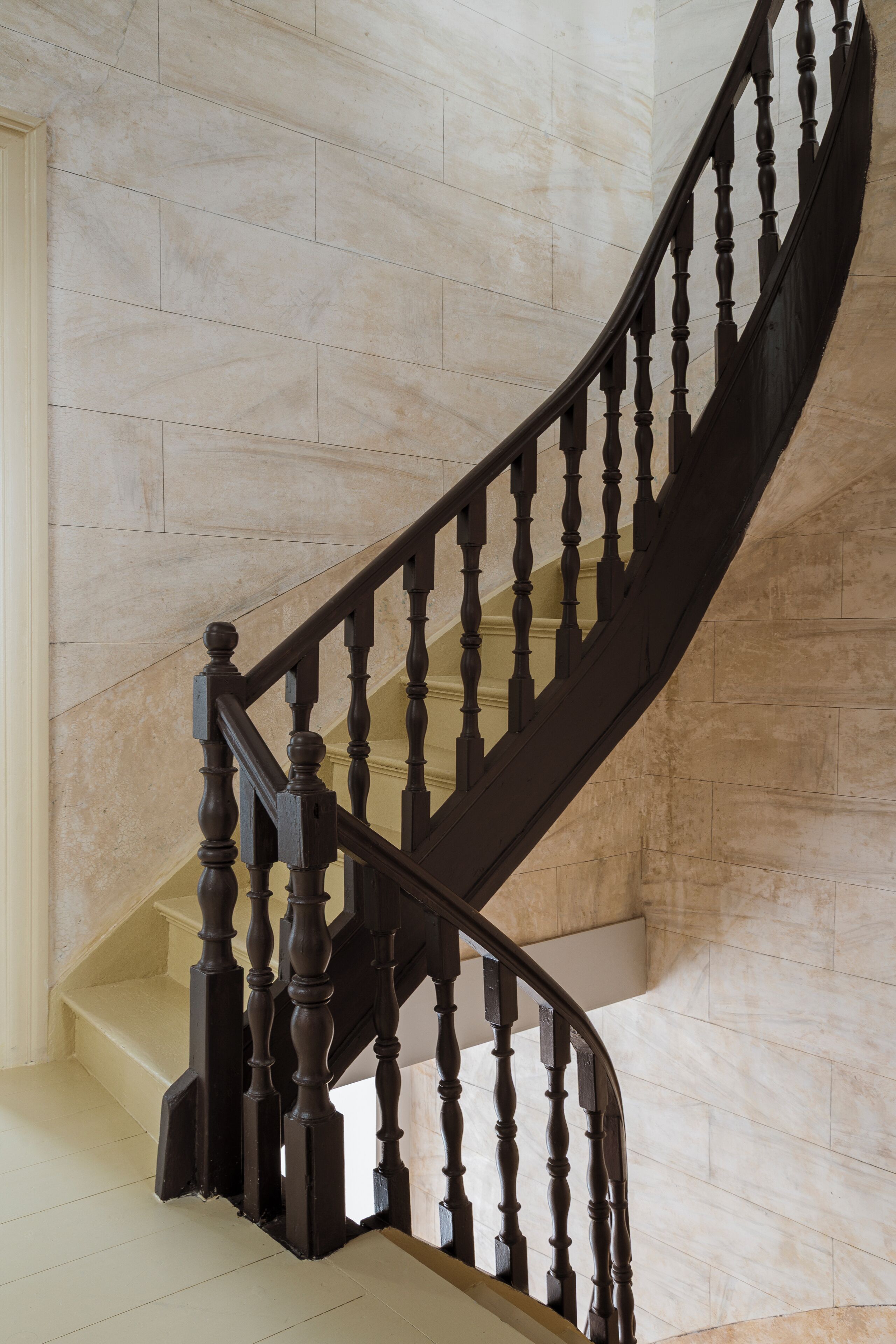 Eine Wendeltreppe mit Holz-Geländern und einer beige gefliesten Wand.