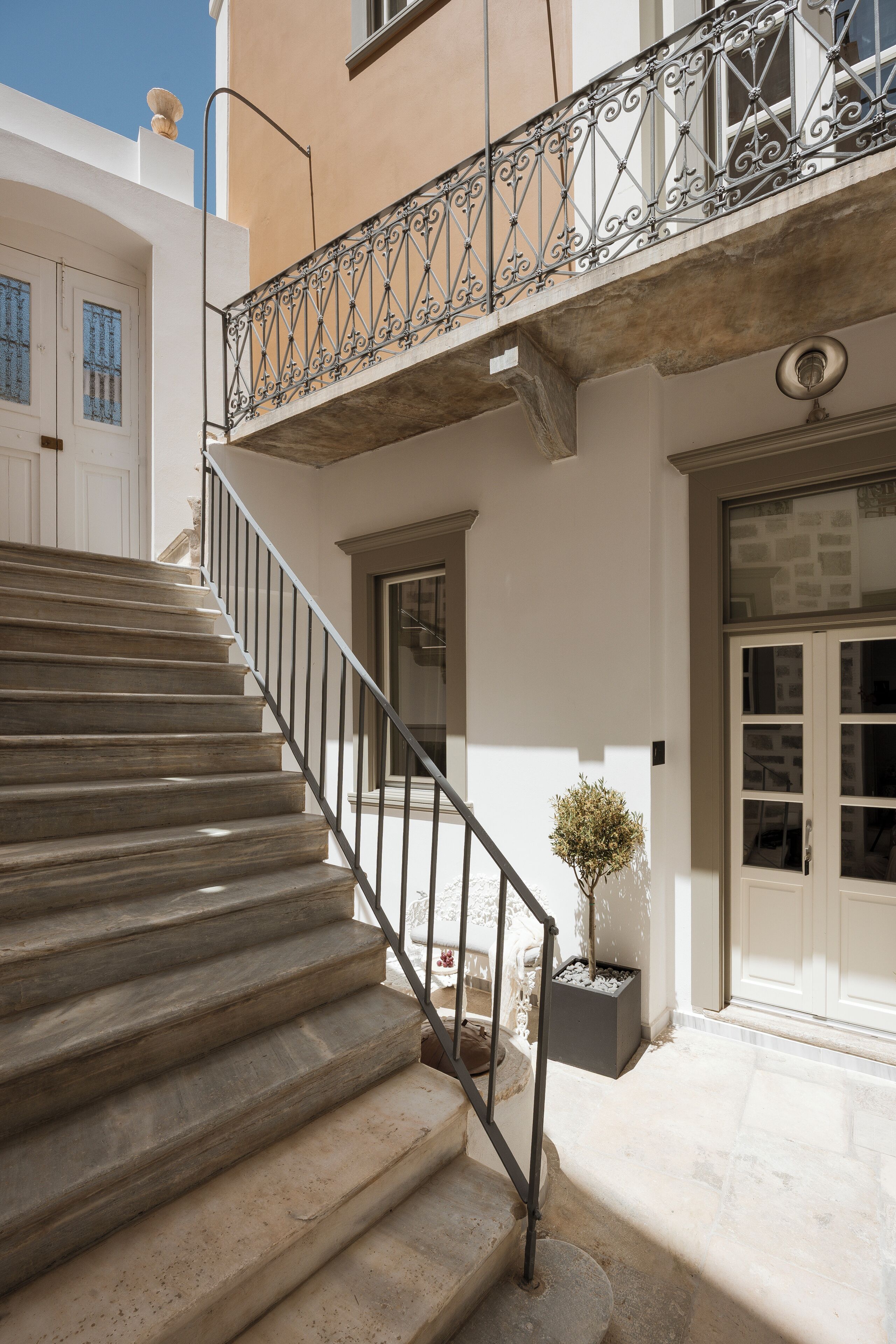 A staircase leading to a balcony with wrought iron railings, a potted plant, and a door with glass panels.