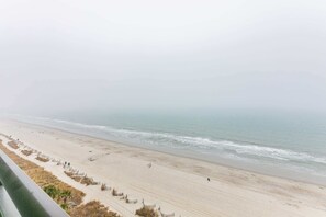 A beach with a sandy shore, a few people, and a fence running parallel to the water. - Oceanview Condo, Pool, Steps to Beach, Hot Tubs (Myrtle Beach)