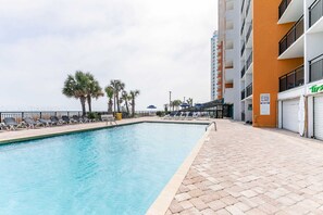 Une piscine avec des chaises longues, des palmiers et un bâtiment doté de balcons.
