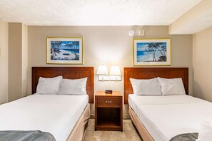 A hotel room with two beds, a nightstand with lamps, and framed beach paintings on the walls.