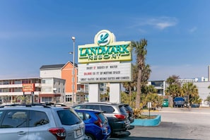 A parking lot with several cars, a sign for Landmark Resort advertising 17 bodies of water, 20,000 sq ft of meeting space, and great rates on rooms, suites, and condos. - Oceanview Condo, Pool, Steps to Beach, Hot Tubs (Myrtle Beach)
