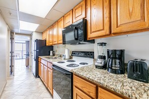 A kitchen with wooden cabinets, a black microwave, a stove, a coffee maker, and a toaster.
