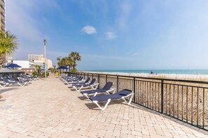 A beachside promenade with sun loungers and umbrellas, a clear sky, and a view of the beach. - Oceanview Condo, Pool, Steps to Beach, Hot Tubs (Myrtle Beach)