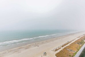 Ein Strand mit sandigem Ufer, einigen Personen und einer Promenade mit Gebäuden entlang des Randes.