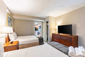 Une chambre d’hôtel avec deux lits, une télévision, une commode en bois et une table de chevet avec une lampe.