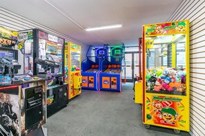 A row of arcade games including 'Road Trip' and 'Toy Soldier' machines, with plush toys in a nearby vending machine.