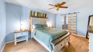 Ein Schlafzimmer mit Bett, Nachttisch, Kommode, Deckenventilator und einer Schiebetür zum Kleiderschrank.