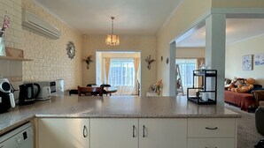A kitchen with a central island, a dining area with a table and chairs, and a living area with a sofa and teddy bears. - Coleman Comfort Hub  - close to City&Air port (Moonah)