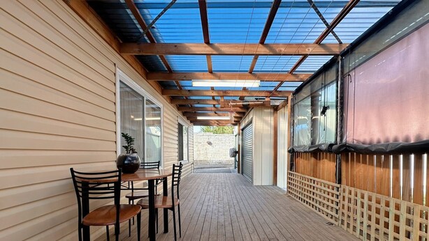 A covered wooden deck with a table and chairs, a potted plant, and a view of the backyard. - Coleman Comfort Hub  - close to City&Air port (Moonah)