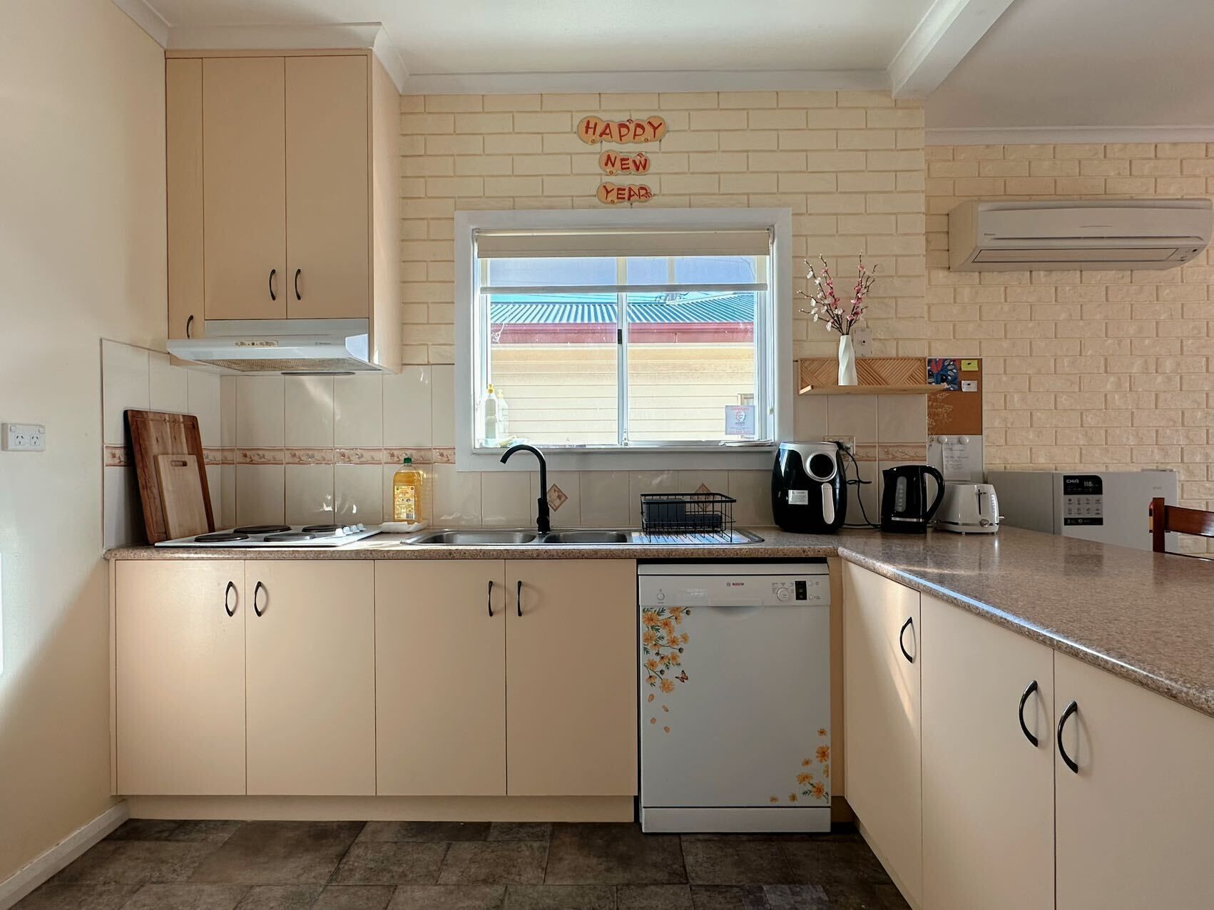 A kitchen with a dishwasher, a coffee maker, and a toaster. There is a window with a view of a building outside.