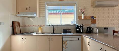 A kitchen with a dishwasher, a coffee maker, and a toaster. There is a window with a view of a building outside.