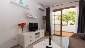 Un soggiorno moderno con TV a schermo piatto, mobili bianchi, un tavolino in vetro e vista su un giardino attraverso una porta scorrevole.