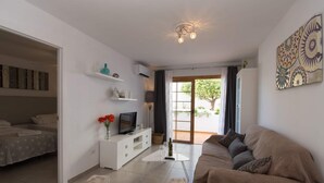 Un soggiorno moderno con un divano, una TV e un tavolino. Si apre una porta su un balcone con vista sul verde.