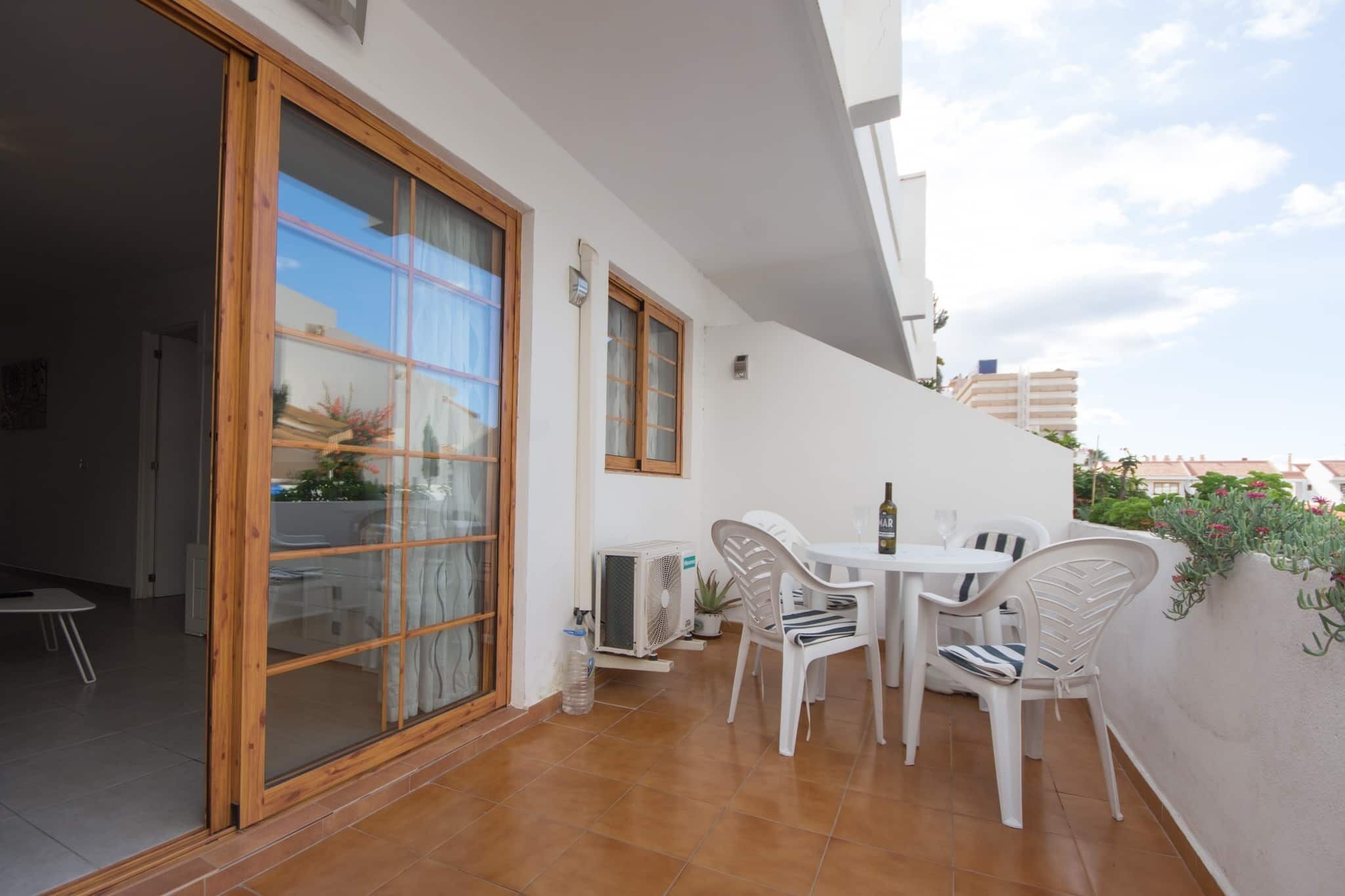 A balcony with a table and chairs, a sliding glass door, and a white wall with a small potted plant.