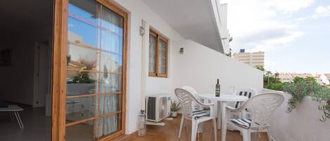 A balcony with a table and chairs, a sliding glass door, and a white wall with a small potted plant.
