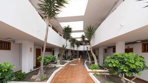 Un ampio cortile interno con pavimento piastrellato, circondato da pareti bianche e diverse aperture.