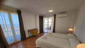 A hotel room with a large bed, a desk, a chair, and a balcony with curtains.