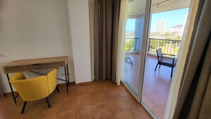 A room with a sliding glass door leading to a balcony with a view of buildings and greenery.