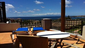 A balcony with a table and chairs, overlooking a coastal view with buildings and a clear sky. - El Rincon 10 - One Bed (Los Cristianos)