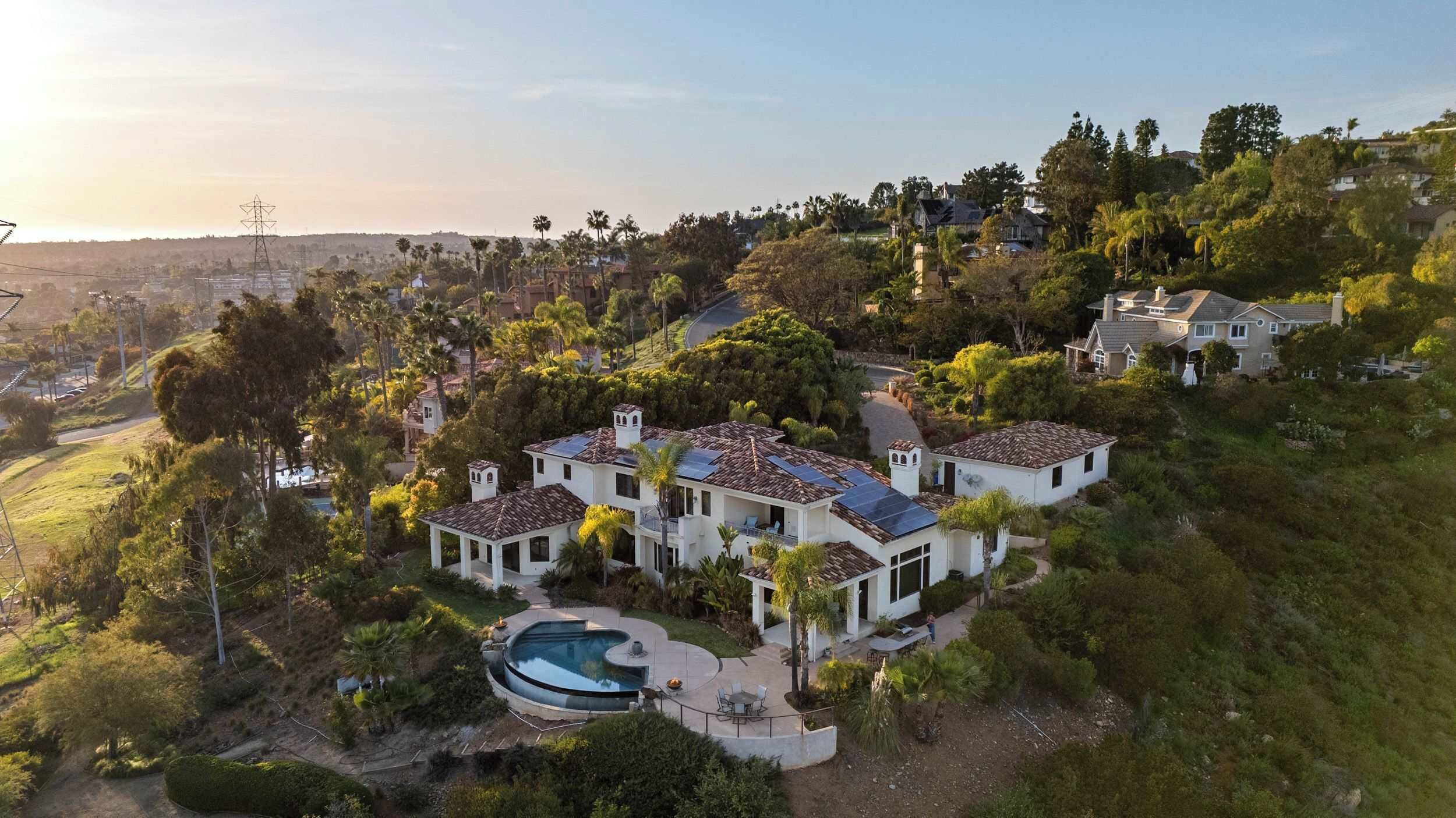 A large, multi-story house with a swimming pool, surrounded by lush greenery and hills.