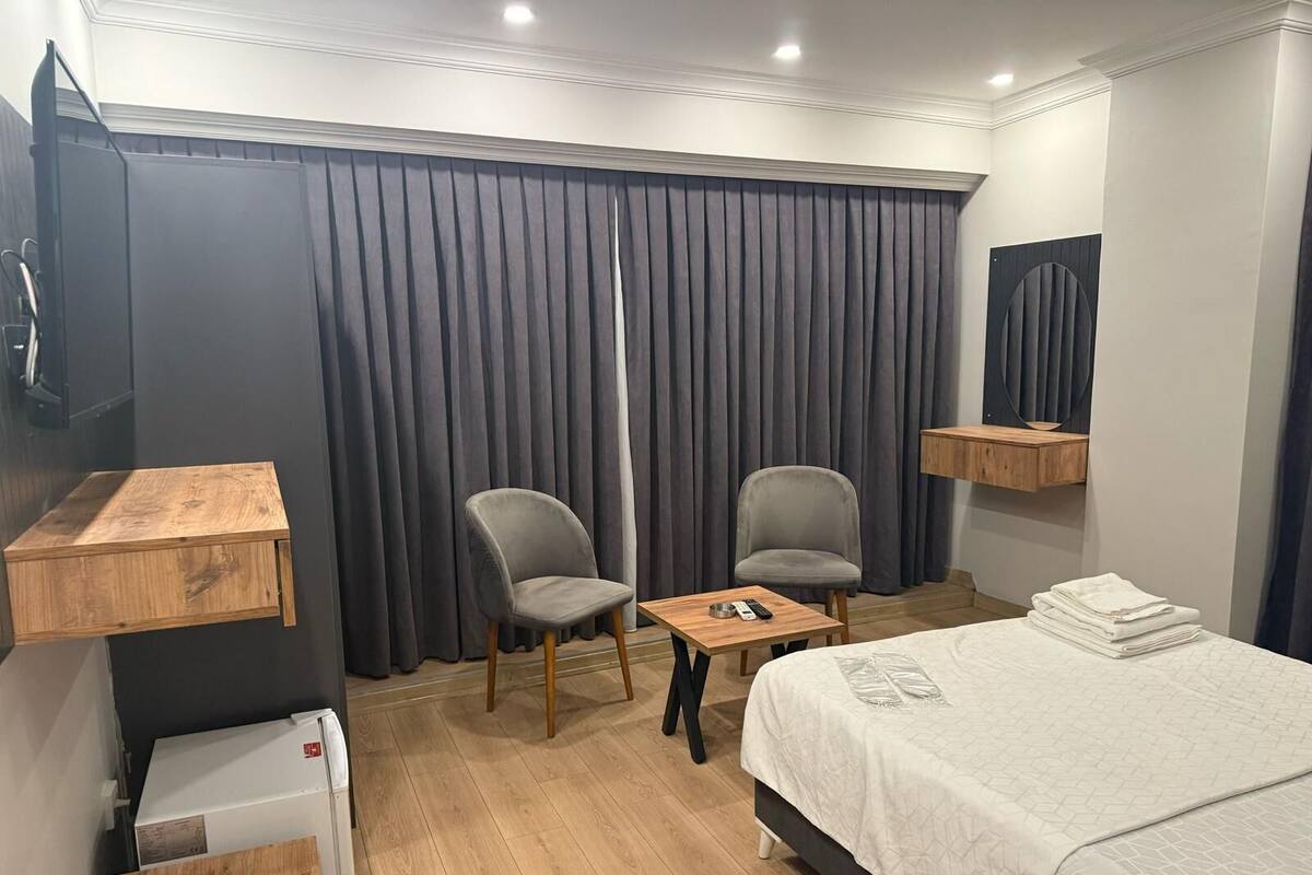 A hotel room with a bed, two chairs, a small table, a TV, and a mirror.