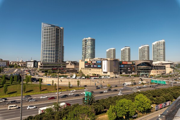 A modern hotel with a glass facade, a prominent Hilton sign, and a view of the surrounding cityscape including a large stadium and high-rise buildings. - Highway 34 Hotel (Istanbul)