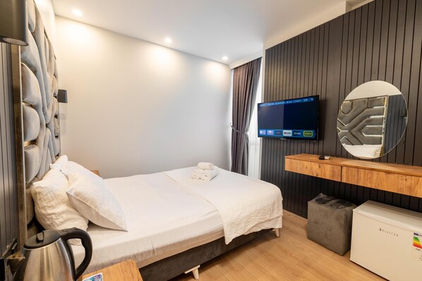 A modern hotel room with a bed, a TV, a mirror, and a minibar.
