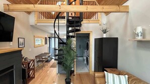 A spacious living area with a fireplace, a leather sofa, a large plant, and a staircase leading to an upper level.