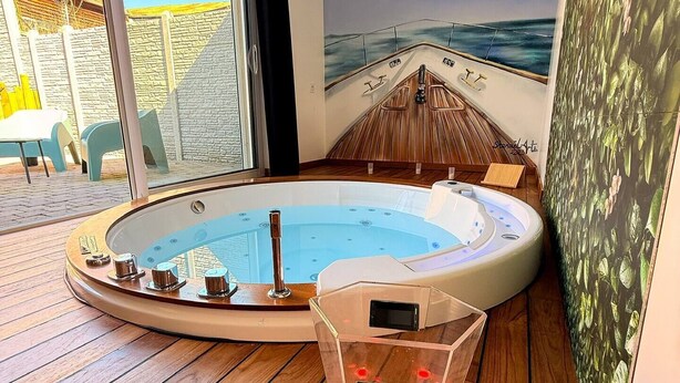Un jacuzzi con cubierta de madera, una puerta de vidrio que da al exterior y un mural de un barco en la pared.