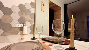 Una mesa de comedor dispuesta con platos, cubiertos y velas, con un salpicadero de azulejos hexagonales y una puerta de madera al fondo.