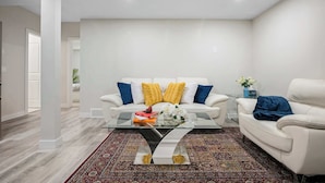 Uma sala de estar moderna com um sofá branco, uma mesa de centro de vidro e um tapete estampado.