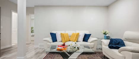 A modern living room with a white sofa, a glass coffee table, and a patterned rug.