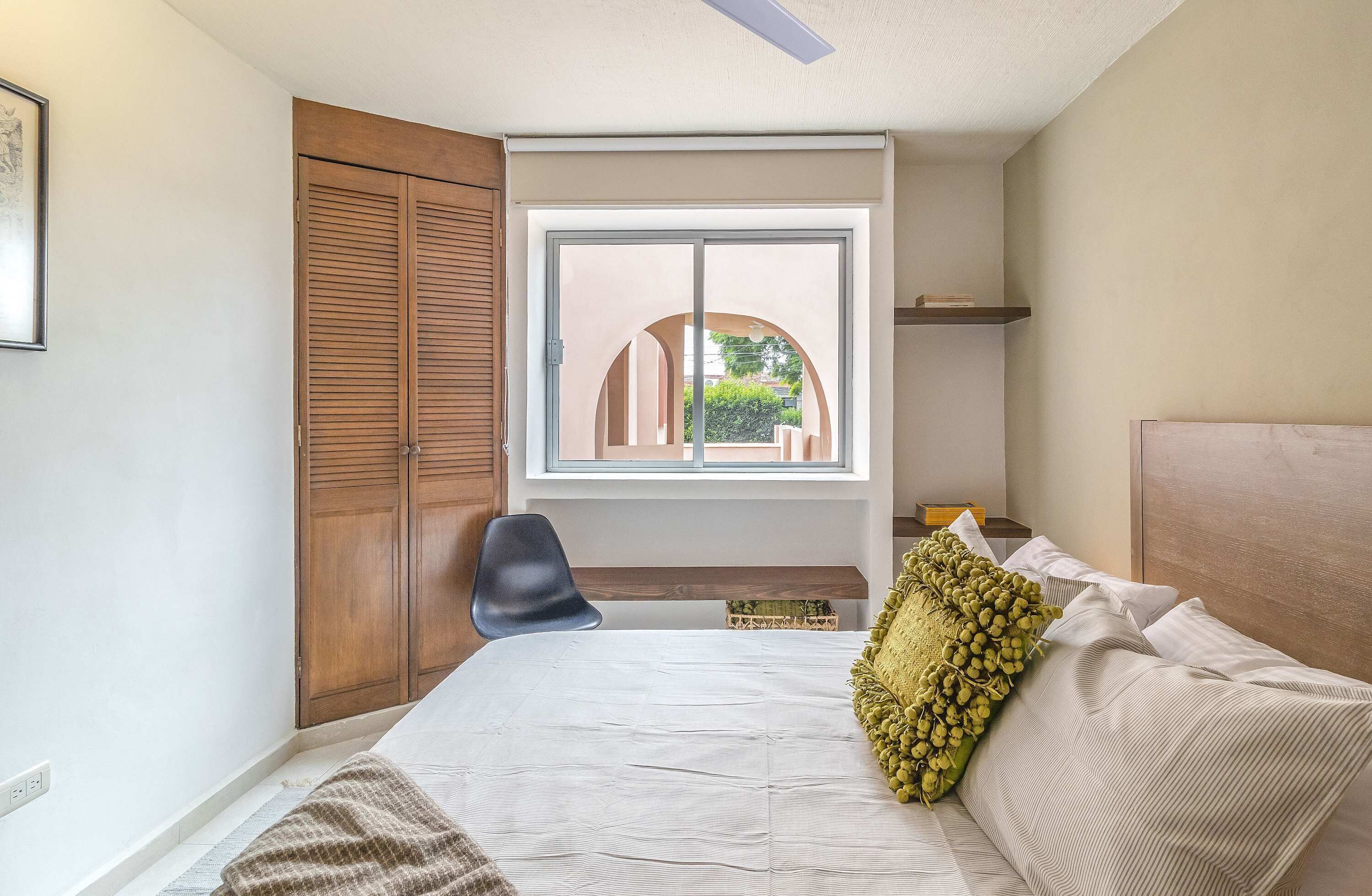 A bedroom with a bed, a chair, a wardrobe, and a window with a view.