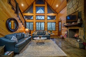 A log cabin interior with a fireplace, a sofa, a coffee table, and a staircase. - Lazy Daze Lodge - Hot Tub and New Custom Playset! (Broken Bow)
