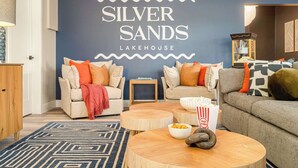 A living room with two sofas, a coffee table, and a wall with 'SILVER SANDS LAKEHOUSE' text. - The Silversands Lakehouse | Hot Tub • Sauna • Game Room (Lansing)
