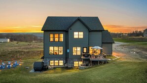 A large two-story house with multiple windows, a porch with outdoor seating, and a well-maintained lawn. - The Silversands Lakehouse | Hot Tub • Sauna • Game Room (Lansing)