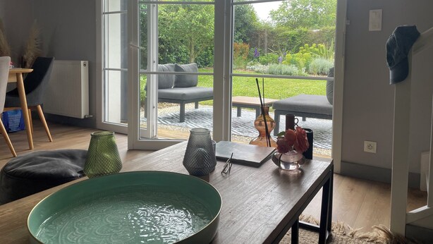 A modern room with a large sliding glass door leading to an outdoor patio. The room features a wooden table with a green bowl, a vase with flowers, and a small lamp. - House in Fouras near Espérance beach  (Fouras)