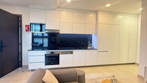 Un salon moderne avec un canapé et une table basse, une cuisine avec des meubles blancs et un plan de travail noir, et une porte en bois.