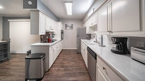 Una cocina moderna con armarios blancos, un basurero de acero inoxidable, una cafetera y un lavavajillas.