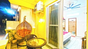 A balcony with wicker furniture, a ceiling fan, and a sliding glass door leading to a patio. - Hotel The Premium Villa Rishikesh (Uttarakhand)