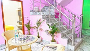 A hotel room with a pink wall, a marble staircase, wicker furniture, and potted plants. - Hotel The Premium Villa Rishikesh (Uttarakhand)