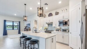 A modern kitchen with white cabinetry, stainless steel appliances, and a large island with bar stools. - Wildblue - William Raveis Rentals (Ft. Myers)