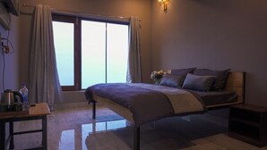 A bedroom with a bed, a bedside table, a nightstand, a window with curtains, and a wall-mounted light fixture.