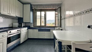 Una cocina con armarios blancos, microondas, horno y ventana con vista a montañas.