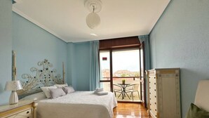 Habitación de hotel con una cama grande, un escritorio con lámpara, una silla y un balcón con vistas.