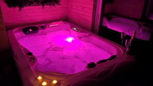 Un jacuzzi con iluminación rosada, una pequeña cascada y velas.